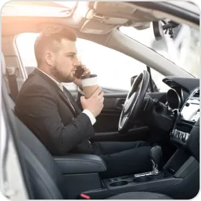 Photo of a man sat in a car on the phone while holding a coffee