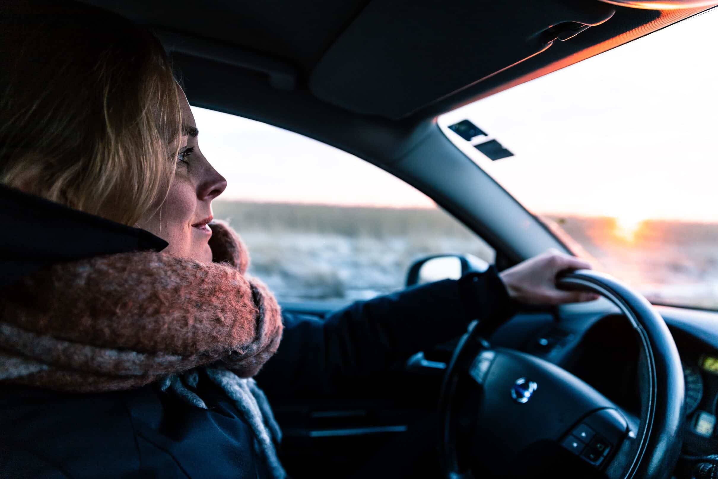 A woman behind the wheel, navigating through a snowy winter landscape.