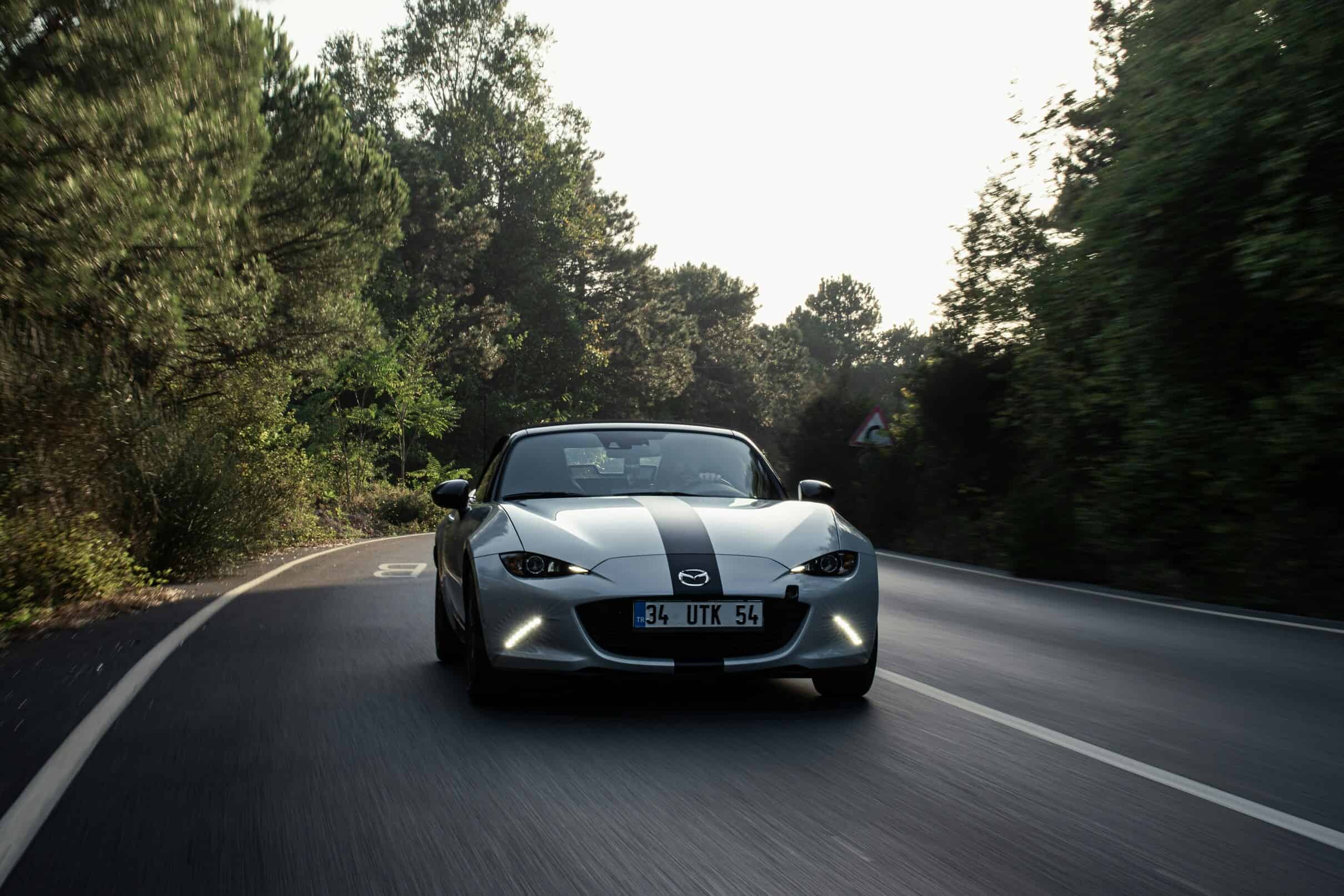 A red Mazda MX-5 convertible parked on a winding road, showcasing its sporty design and open-top motoring experience.