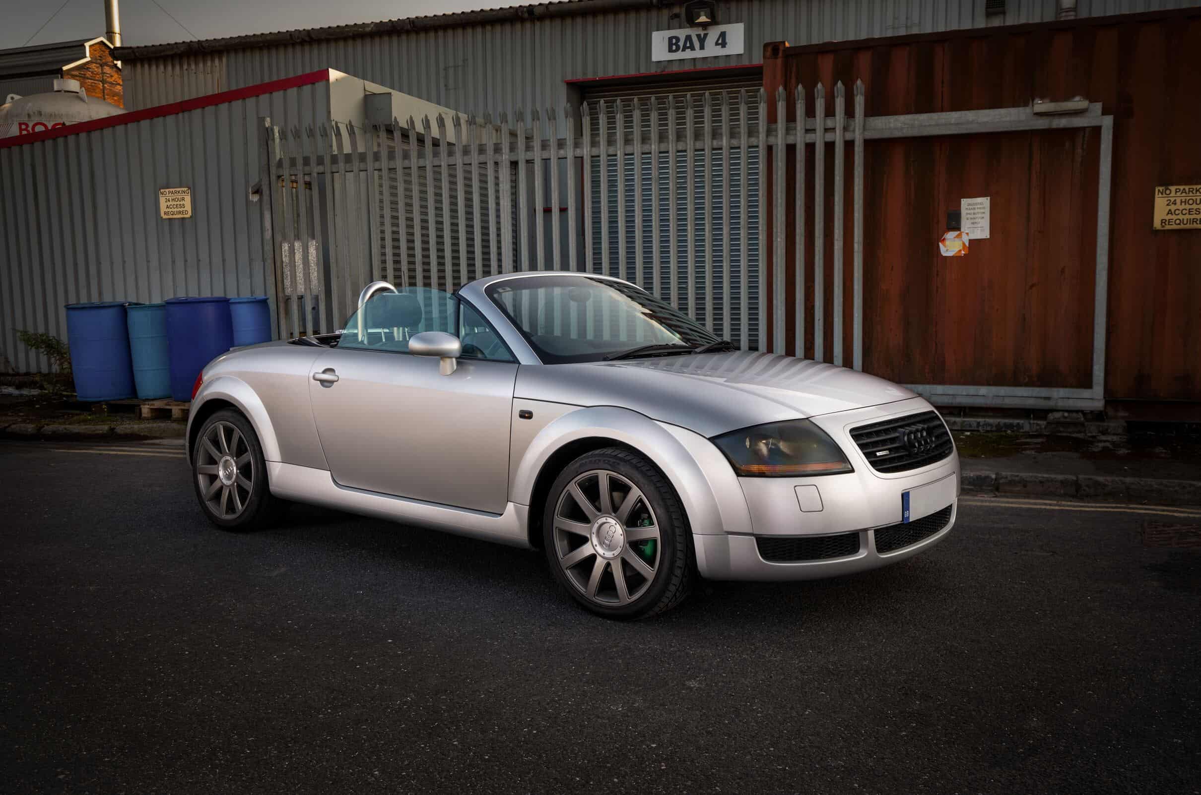 A silver Audi TT coupe parked in an urban setting, highlighting its sleek lines and modern design features.