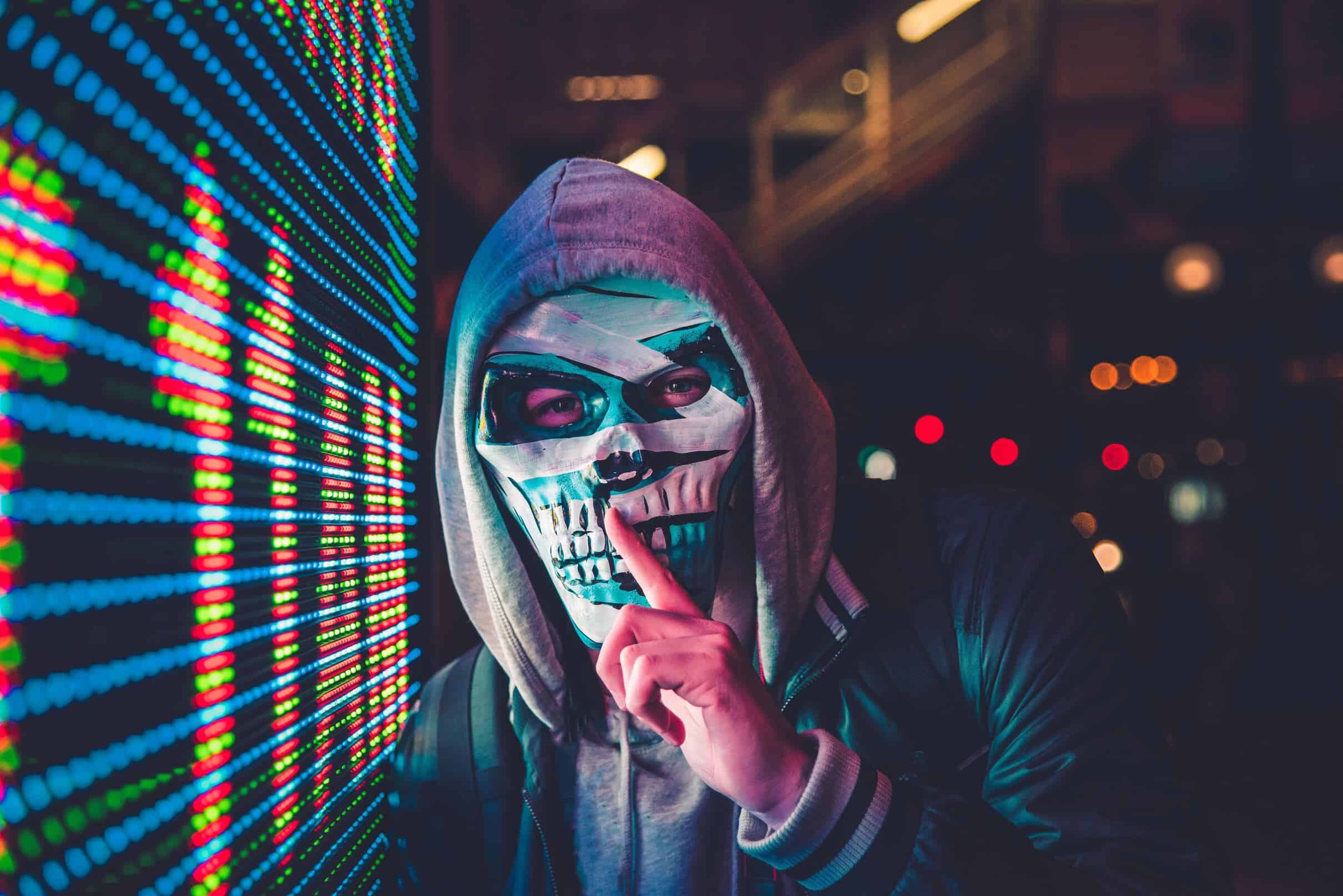 Image depicting a person in front of a computer, posing as a hacker with a hood, typing on a keyboard.