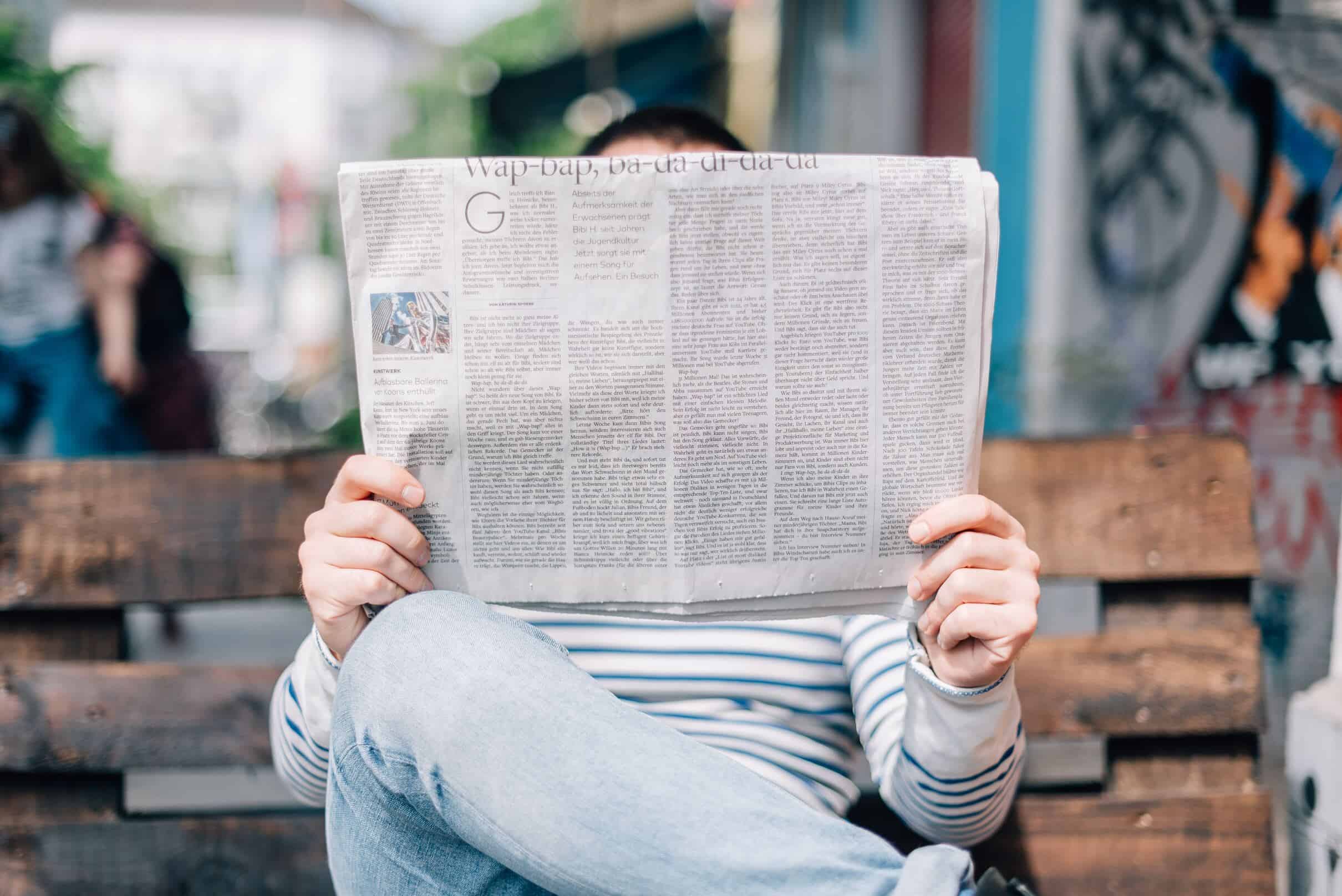 A person reading a newspaper, absorbed in its contents while seated in a relaxed posture, showcasing the pleasure of staying informed through print media.